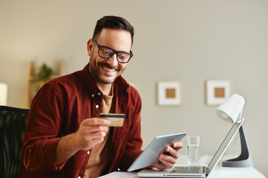 Young man holding credit card and tablet at home at table